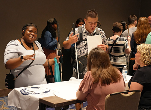 Chrichelle Brown smiles and speaks with a career fair table. Mason Fessenden stands next to her.